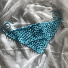 a blue crocheted triangle laying on top of a white bed sheet covered in sheets