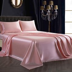 a bed covered in pink sheets and pillows next to a window with chandelier