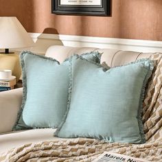 two blue pillows sitting on top of a white couch next to a lamp and pillow case