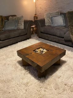 the square walnut stained table is on display in front of two couches and a fireplace