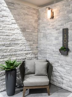 a chair sitting in front of a white brick wall next to a potted plant