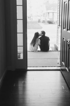 two people are sitting on the floor in front of an open door and looking at each other