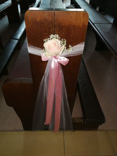 a chair with a pink ribbon and flower on the seat belt, sitting in front of pews