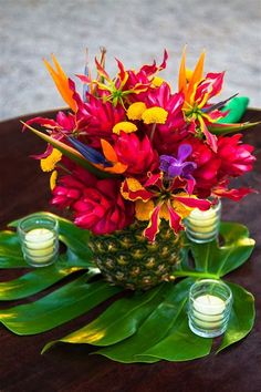 a pineapple vase filled with colorful flowers on top of a wooden table next to candles