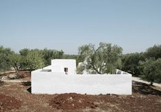 a white building sitting on top of a dirt field next to trees and bushes in the background