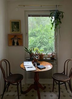 two wooden chairs sitting at a table in front of a window with potted plants on it