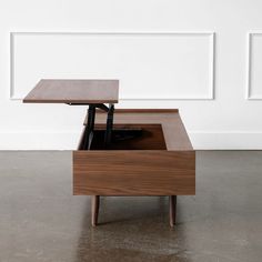 a coffee table with an open drawer on the bottom and one shelf below it, in front of a white wall