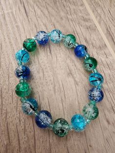 a blue and green beaded bracelet sitting on top of a wooden table