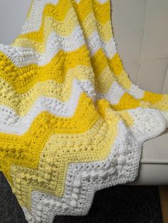 a yellow and white crocheted blanket sitting on top of a couch