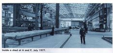 an old black and white photo of a man walking in a factory with lots of machinery