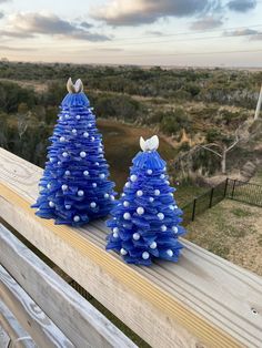 two blue plastic christmas trees sitting on top of a wooden bench next to a field