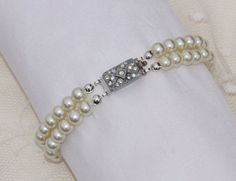 "A stunning vintage bracelet made during the art deco era. This is a two strand bracelet made with very soft white colored glass pearls. The pearls are in wonderful vintage condition and have a great luster and shine! Pearls are 6mm in size and connect to a paved, rhodium plated tongue and groove clasp. The tongue and groove clasp does have two small silver push points on the side, which is not shown in the photos. The pearls have been re-strung onto new, strong silk cording so you can ensure it