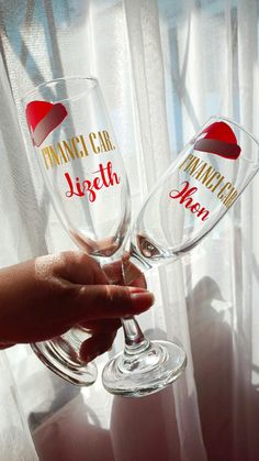 two wine glasses with red hearts on them are being held by someone's hand