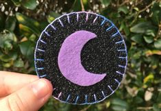 a hand holding up a purple and black patch with the letter c on it's side