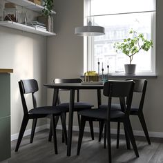 a dining table with four chairs and a potted plant in the window sill