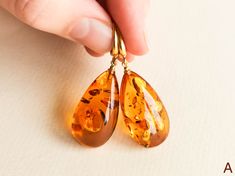 "Light orange natural amber earrings for women that love bright eye-catching colors. These drop shape genuine amber earrings brighten up your eyes. And we've heard - some lives too! Even though they are in cognac color, all they do is sweetens your life. MATERIALS AND SIZE: Stone: 100% Natural Baltic Amber Findings: Sterling silver 925 gold plated Earrings A: Weight: 7 g (0,324 oz) Bead size: 3 cm (1,18 in) x 1,6 cm (0,62 in) Total earring length:4,7 cm (1.85 in) Earrings B: Weight: 8,4 g (0,29o Orange Baltic Amber Teardrop Jewelry, Baltic Amber Teardrop Earrings For Gift, Baltic Amber Teardrop Earrings As Gift, Hypoallergenic Amber Teardrop Jewelry, Amber Earrings For Gift, Baltic Amber Earrings As A Gift, Gift Amber Drop Earrings, Amber Teardrop Earrings As A Gift, Amber Teardrop Earrings Gift