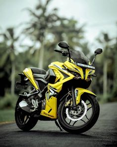 a yellow and black motorcycle parked on the side of a road next to some trees