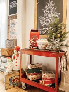 a christmas tree is on top of a red cart in front of a chalkboard