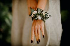 a woman's hand with flowers and greenery on her wrist, wearing a white dress