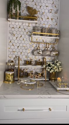 a white and gold kitchen with shelves filled with dishes, cups and vases on the counter