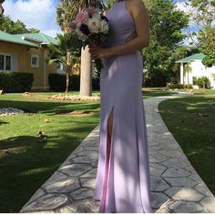 a woman in a long purple dress holding a bouquet and posing for the camera outside