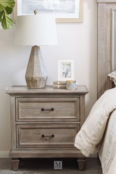 a nightstand with two drawers and a lamp on it next to a bed in a bedroom