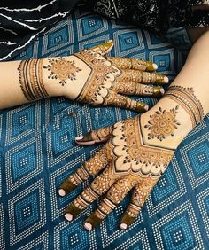 two hands with henna tattoos on them sitting next to each other in front of a blue blanket