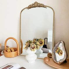 a mirror sitting on top of a desk next to a vase with flowers in it