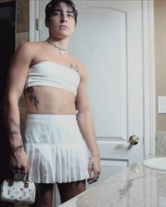 a woman in a white dress holding a purse and standing next to a bathroom sink