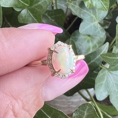 a woman's hand holding a ring with an opal in the center and diamonds around it