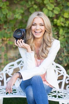 a woman sitting on a bench holding up a camera