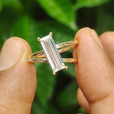 a person holding a ring with a baguette cut diamond in it's middle