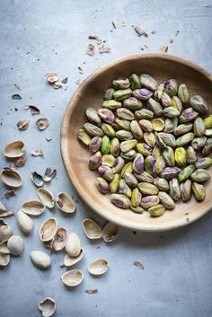 a wooden bowl filled with pistachios on top of a blue countertop