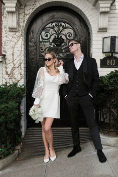 a man and woman standing in front of a black door with white flowers on it