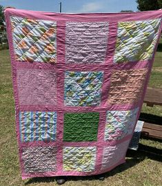 a pink and green patchwork quilt sitting on top of a wooden bench in the grass