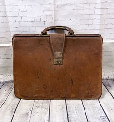 an old brown suitcase sitting on top of a wooden floor next to a brick wall