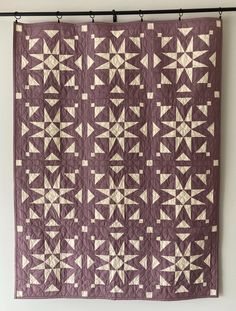 a purple and white quilt hanging on a wall