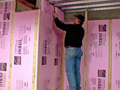 a man in black shirt and jeans standing next to pink wall with insulation on it