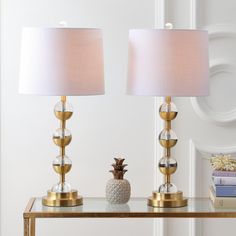 two lamps sitting on top of a glass table next to a white vase with pineapples