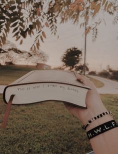 a hand holding an open book with writing on it in front of a grassy field