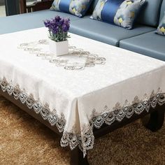 a white table cloth on top of a blue couch with purple flowers in a vase