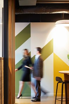 two people are walking in an office with yellow and green stripes on the wall behind them