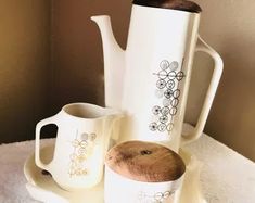 there are three coffee mugs and one teapot on the table with white towels