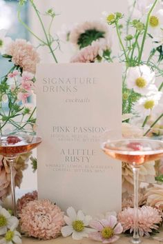 a table topped with two wine glasses filled with pink and white flowers next to a menu