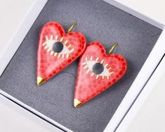 two red heart shaped earrings with gold spikes and eyeballs on them in a box