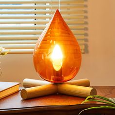 an orange light bulb sitting on top of a wooden table next to books and a plant