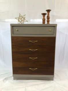 a wooden dresser with four drawers and two candles on top, against a white backdrop