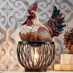 a rooster figurine sitting on top of a table next to a book and lamp