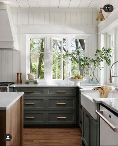 a kitchen with wooden floors and green cabinets, white walls and windows that look out onto the woods