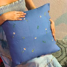 a woman is holding a blue pillow with daisies on it and her hands are resting on the pillow